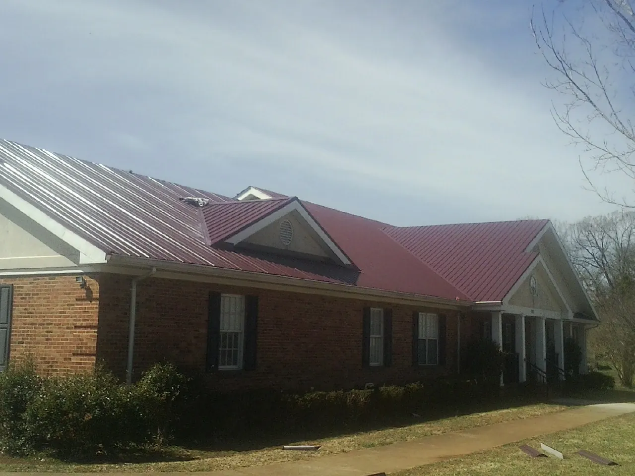 Red metal roof with gabled entries on a long brick building, from a Hail Damage Roof Repair job in Waterford